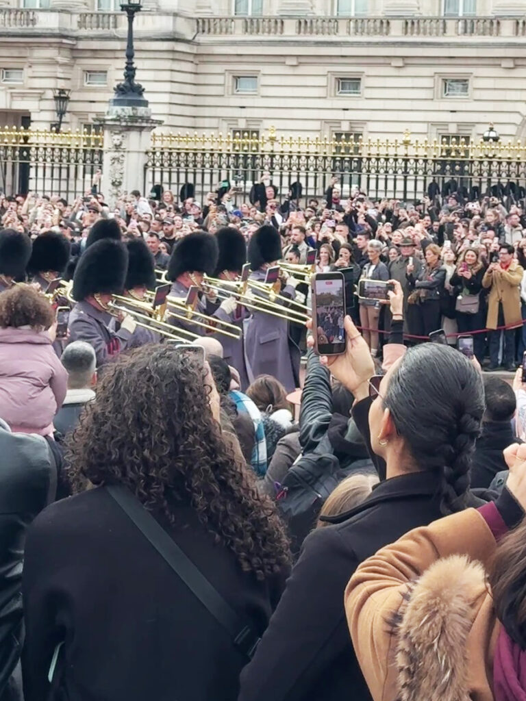 ベアスキン帽とグレーの外套を着た楽隊の衛兵が演奏しながら行進する様子